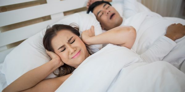 Portrait of woman blocking ears with man sleeping snoring on bed
